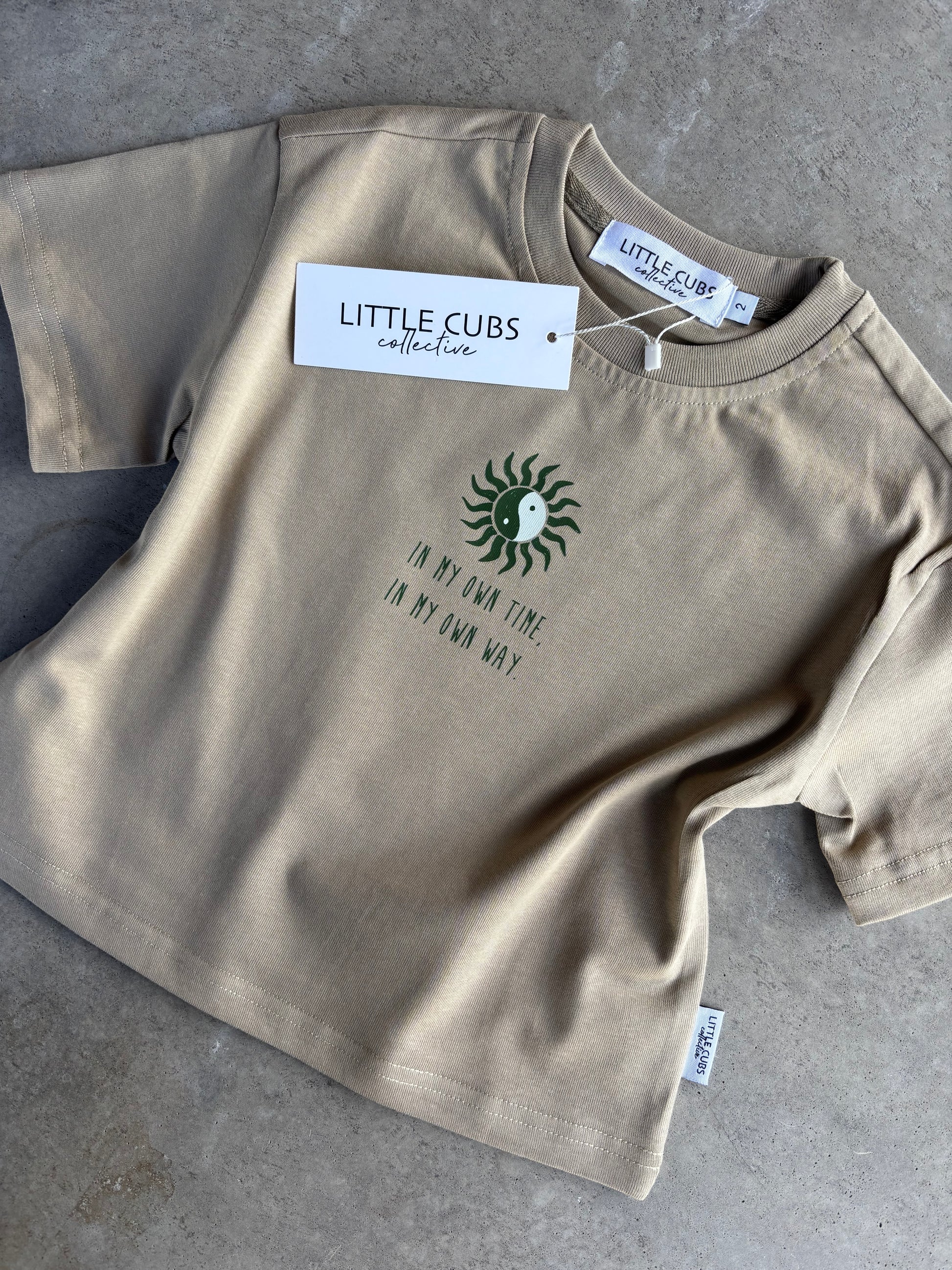 Flat lay taupe colour, boxy fit tee with placement print in my own time, in my own way. with tag Little Cubs Collective. 