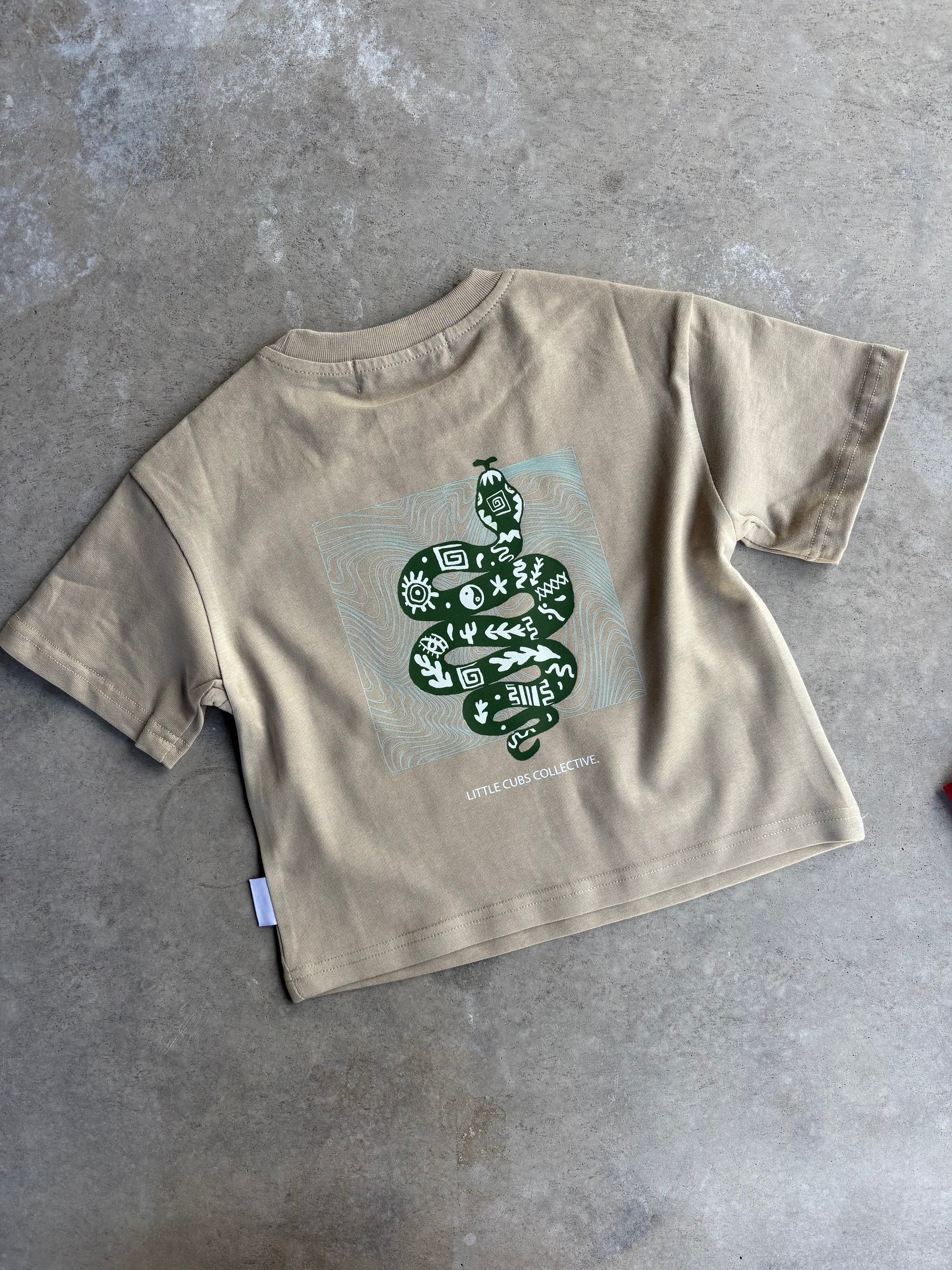 flat lay of beige colour kids tee. Back graphic of snake with handdrawn symbols. boxy fit and oversized. 