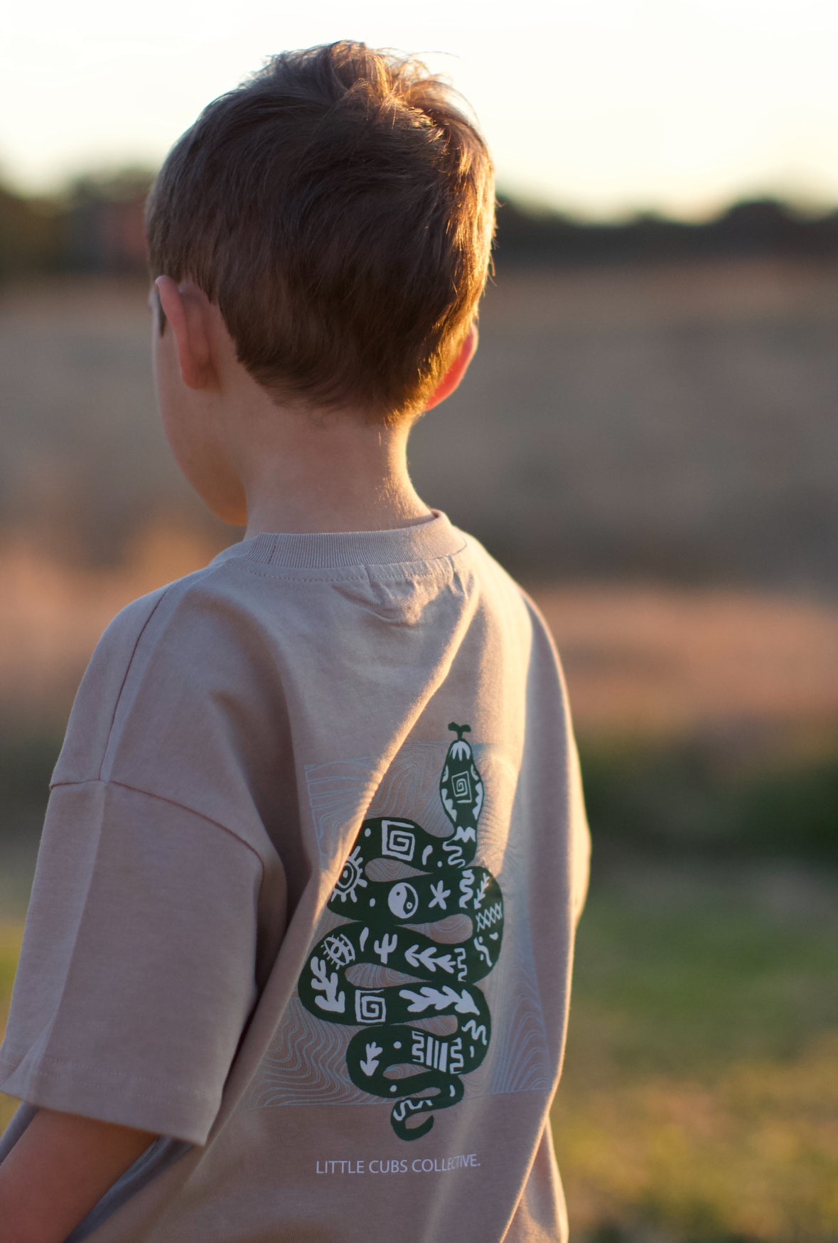 close up photo of the in my own way tee on a child with the image of a handrawn snake and symbols inside of the snake and small logo little cubs collective below the print.