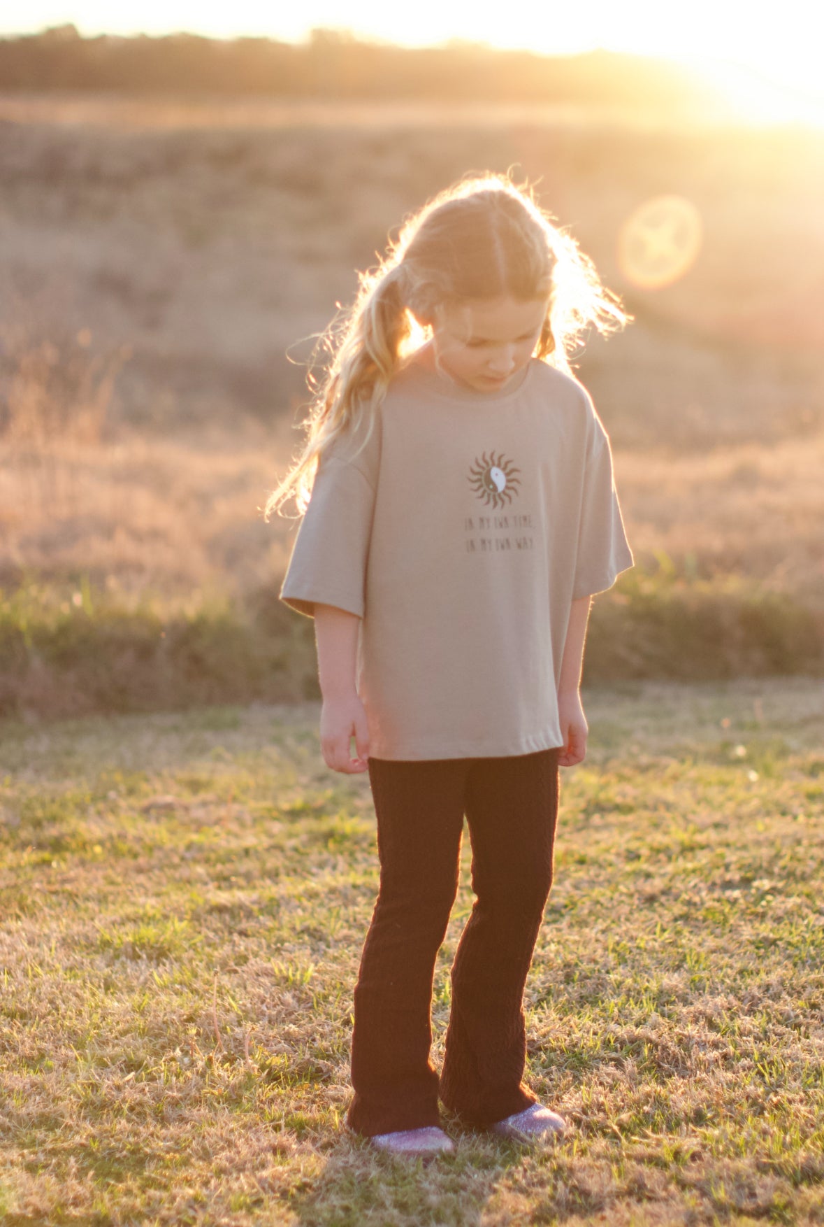 candid moment of child wearing In my own way tee in a park with sun glowing behind. 